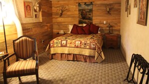 Une chambre avec un mur en bois, un lit recouvert d’une courtepointe, une chaise, une table de chevet et une lampe.