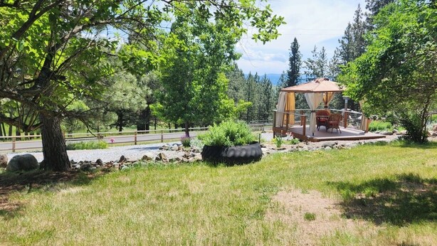 Un belvédère doté d’une terrasse en bois, entouré d’une pelouse agrémentée d’arbres et d’un sentier pavé de pierres.