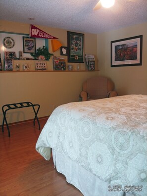A room with a bed, a chair, a shelf with memorabilia, and a framed picture on the wall.