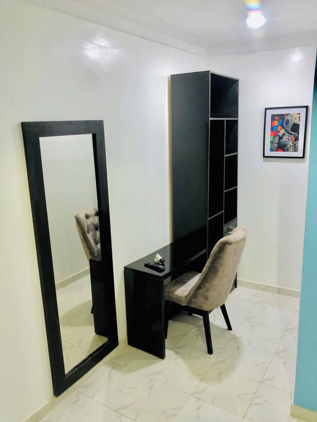 Una habitación con un mueble bajo negro para el televisor, una silla, un espejo grande y un cuadro en la pared.