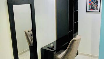 Una habitación con un mueble bajo negro para el televisor, una silla, un espejo grande y un cuadro en la pared.