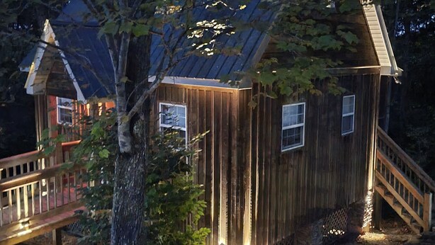 A wooden cabin with a metal roof, a wooden deck, and a staircase leading to the entrance. - Cozy Cabin (Burnside)