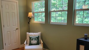 A room with a wooden floor, a chair with a pillow, two windows, a door, and a lamp. - Cozy Cabin (Burnside)