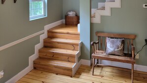 A staircase with wooden steps leading to a landing, a window with a view of greenery, and a bench with a cushion. - Cozy Cabin (Burnside)