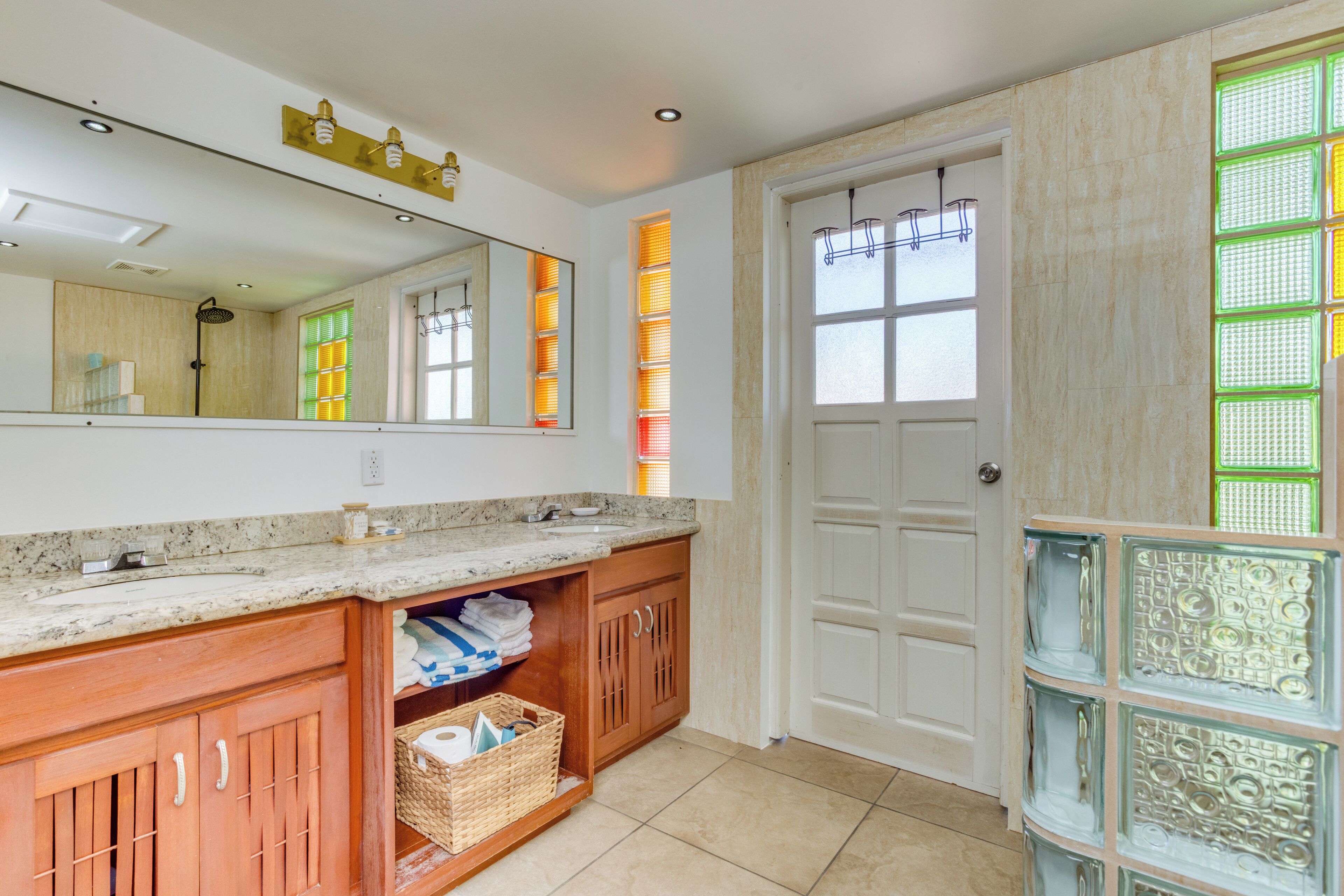 A bathroom with a double sink, wooden cabinets, a mirror, and a door with a window.