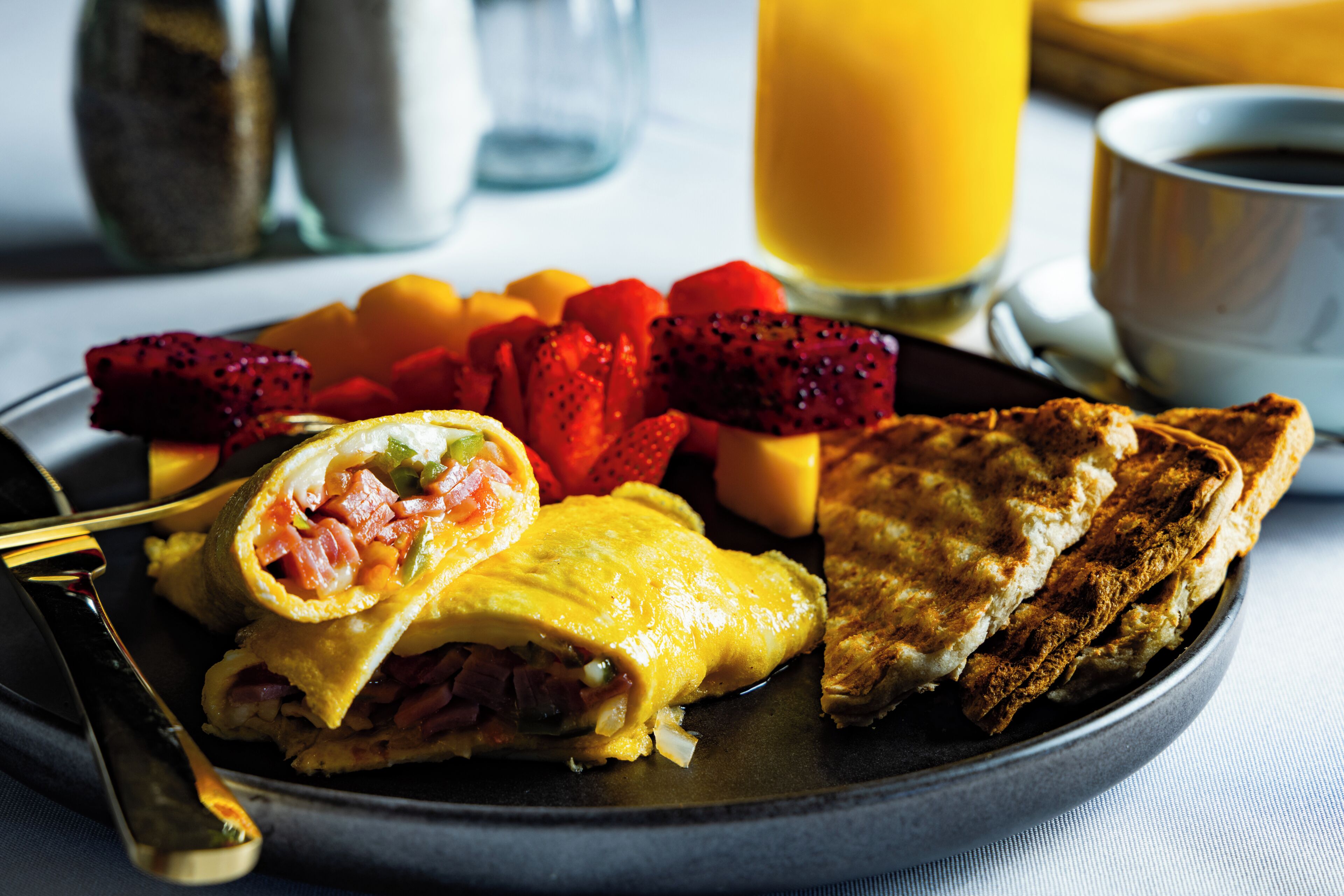 Een ontbijtbord met eieren, ham en groenten, vergezeld van fruit en toast.