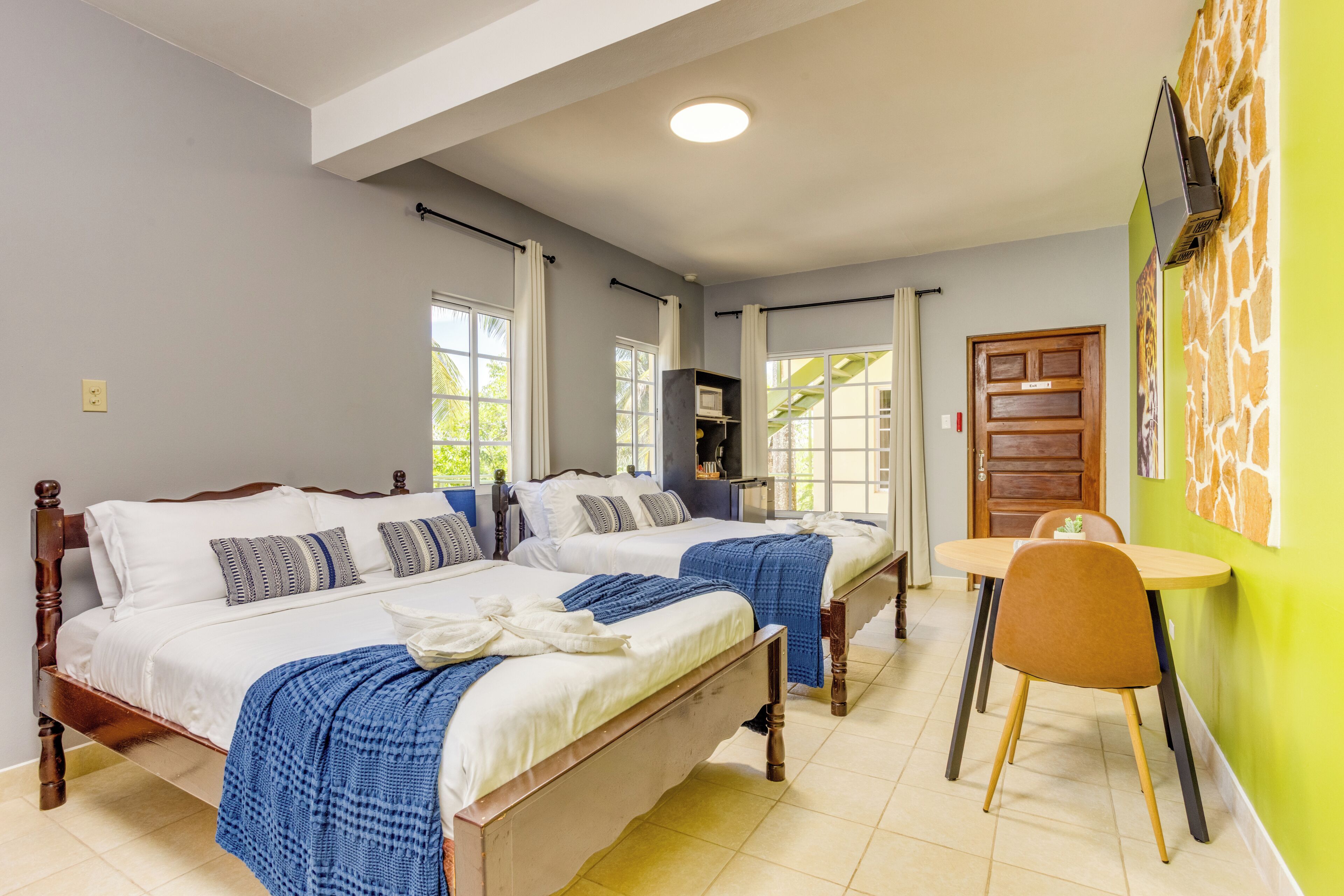 A hotel room with two beds, a dining table, and a green accent wall.