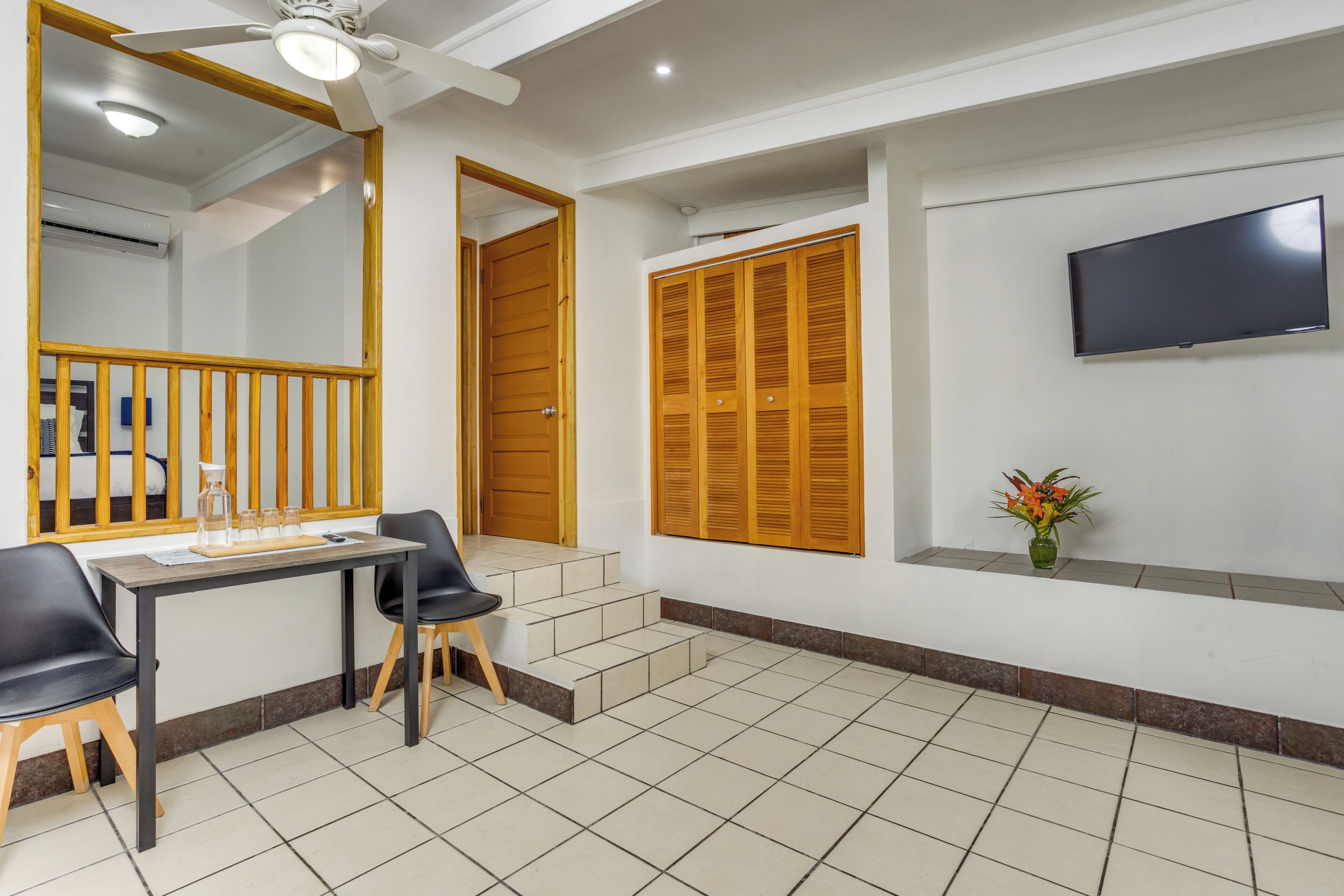 A room with a desk, chairs, a TV, a wooden door, and a staircase.