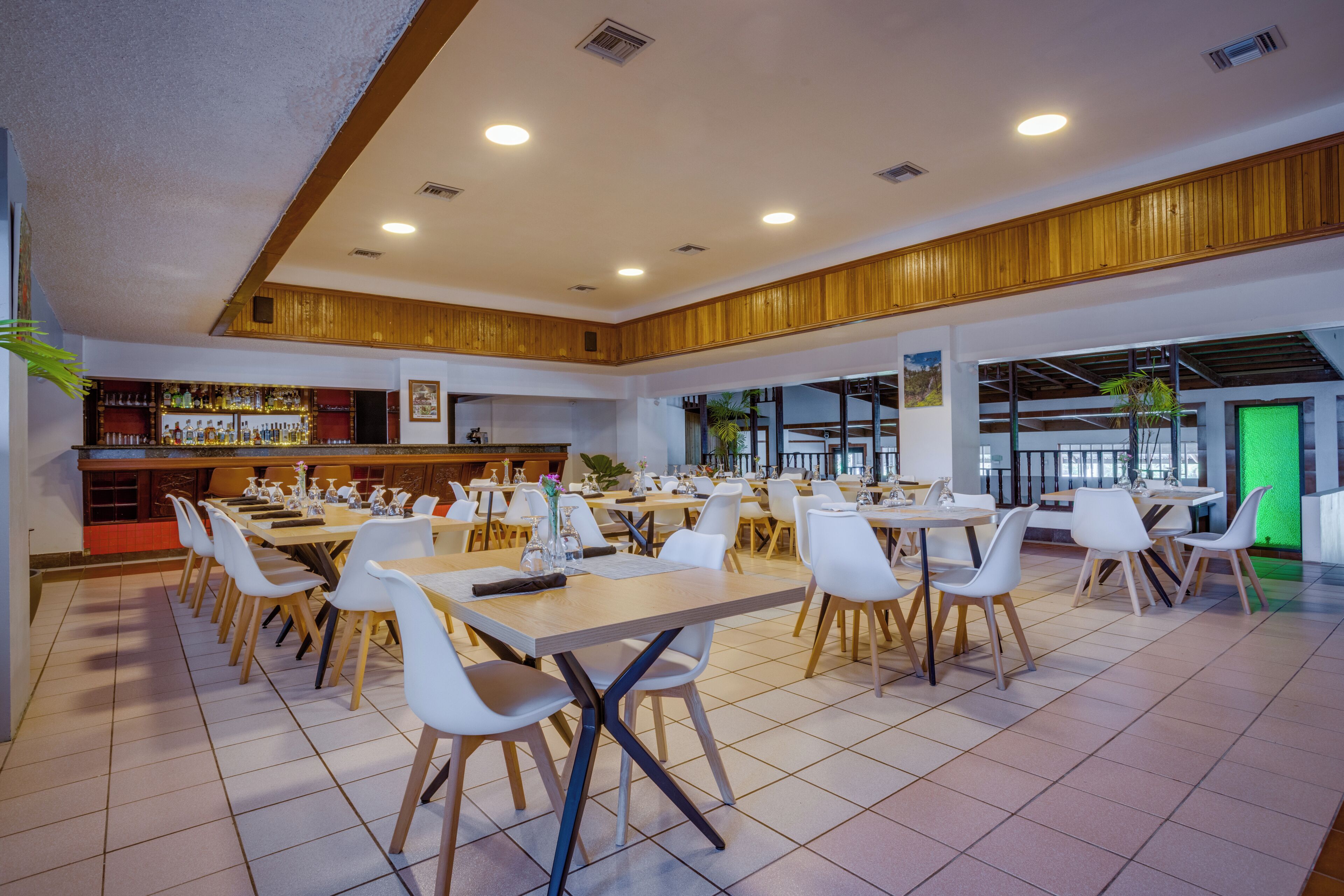 A spacious dining area with multiple tables and chairs, a bar area, and large windows allowing natural light.