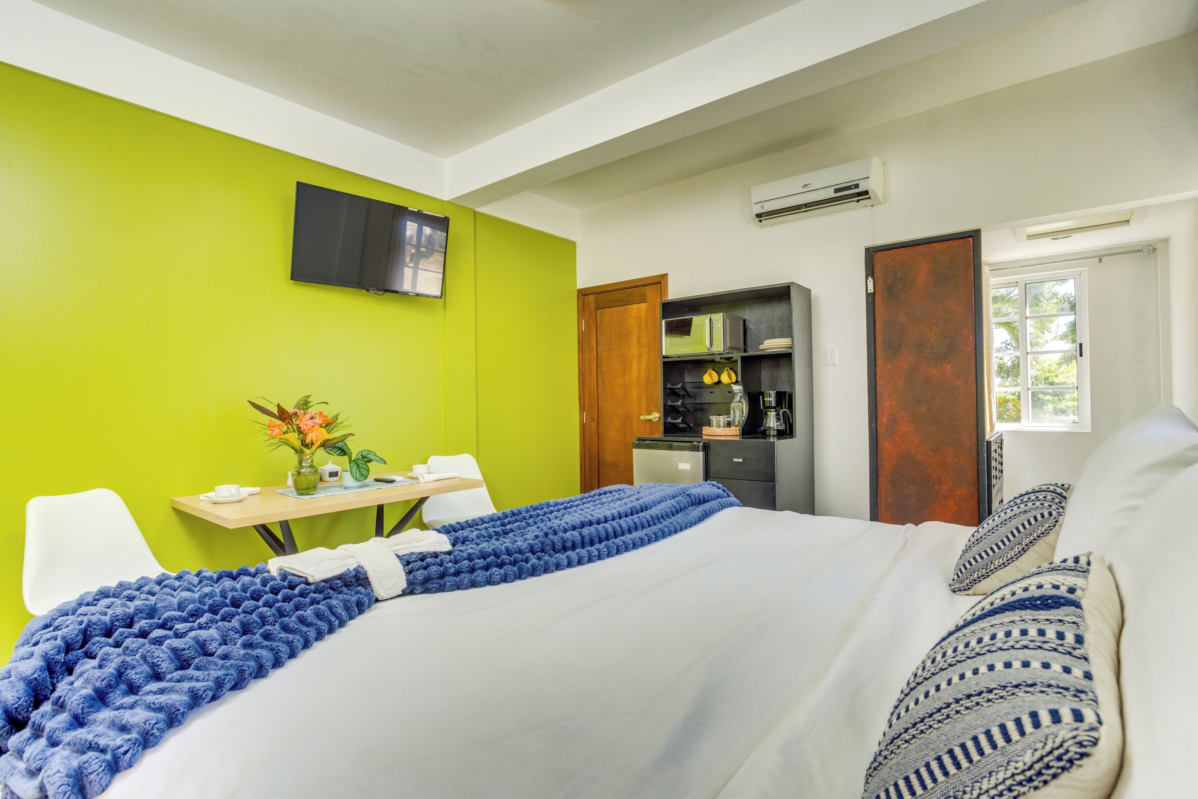 A hotel room with a bed, a desk, a chair, a TV, an air conditioning unit, and a window.