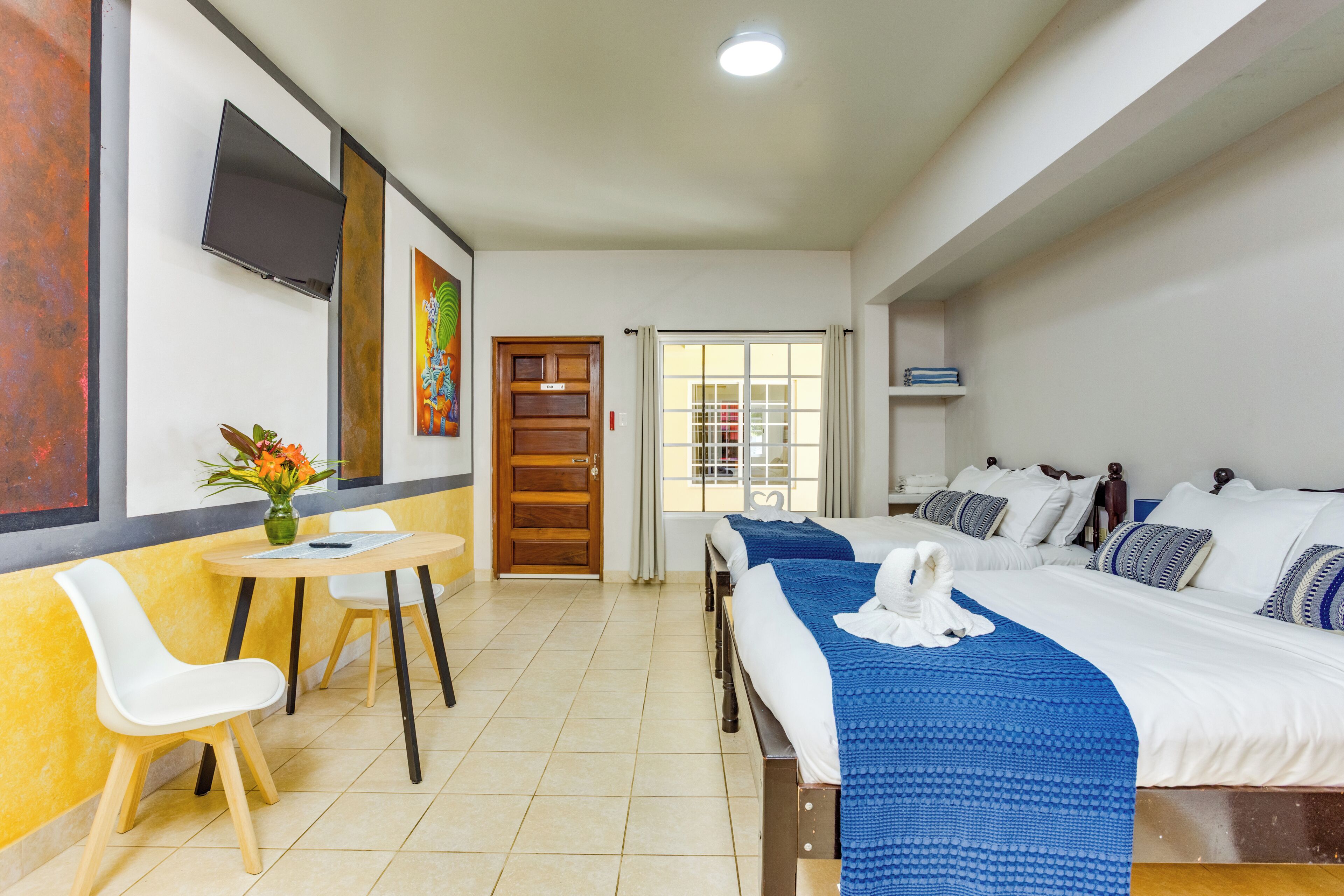 Habitació d'hotel amb llit, escriptori, cadires, televisió i obra d'art a les parets.
