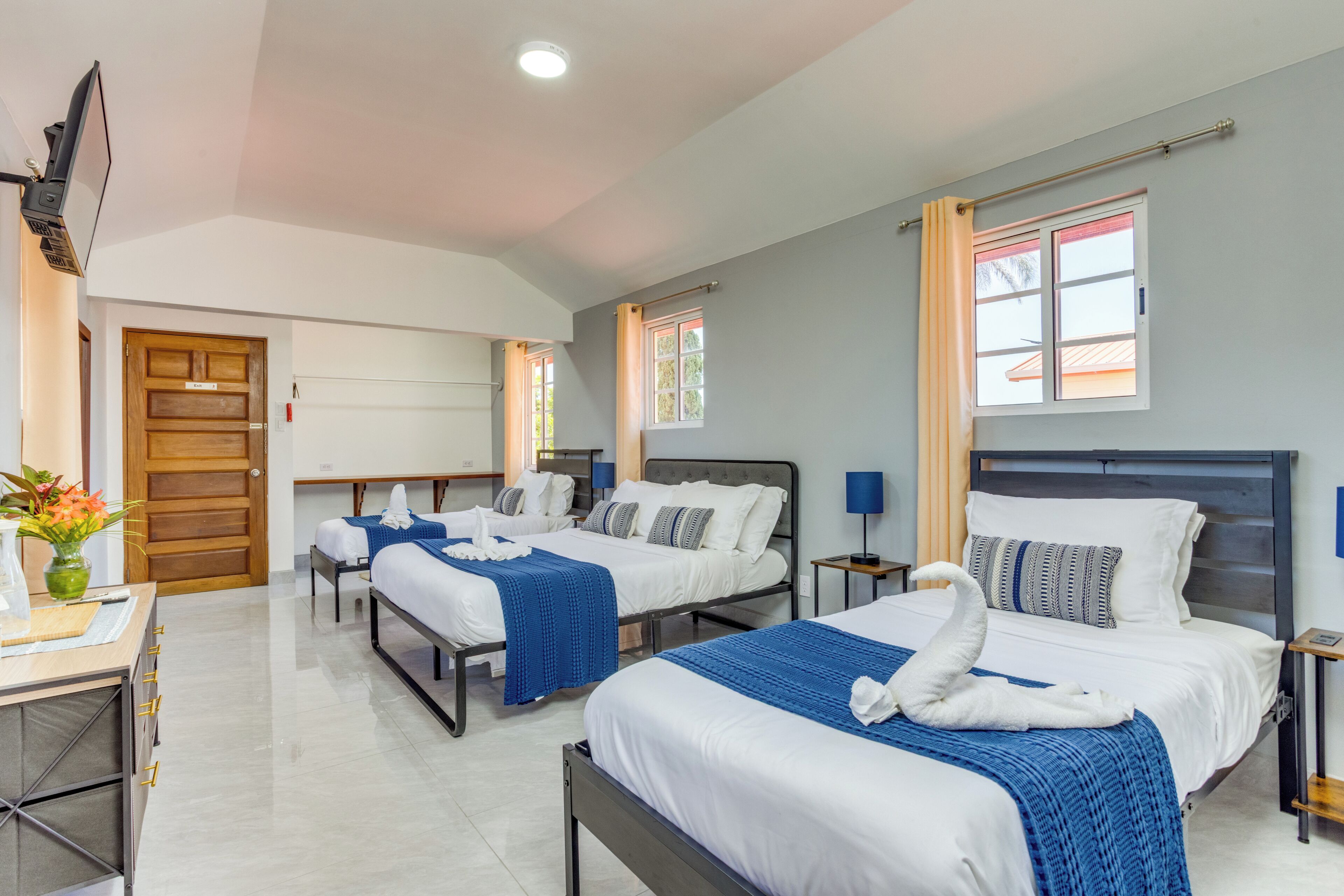 Camera d'albergo con tre letti, una scrivania, una TV e una finestra con tende.