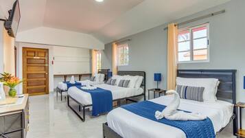 Camera d'albergo con tre letti, una scrivania, una TV e una finestra con tende.