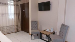 Habitación de hotel con una cama, dos sillones, una mesita con cafetera y un televisor en la pared.