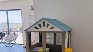 Ein Spielbereich für Kinder mit einem kleinen Holzspielhäuschen, bunten Stühlen und einem Tisch.