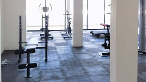 Ein Fitnessstudio mit unterschiedlichen Trainingsgeräten, großen Fenstern und einem Betonboden.