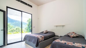 Un dormitorio moderno con dos camas, un ventanal corredero que da a un balcón y vistas al verdor.