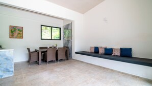 Una habitación amplia con zona de comedor, un banco empotrado con cojines y un ventanal grande.
