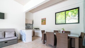 Un moderno espacio de sala con sofá, mesa de comedor y sillas, una zona de cocina y un amplio ventanal con vista a zonas verdes.