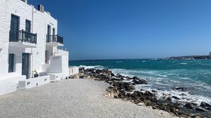 A white building with balconies overlooking a rocky shoreline and the sea.
