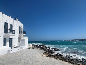Um edifício branco com varandas voltadas para uma costa rochosa e o mar.