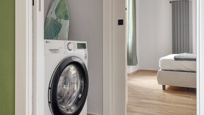 A modern laundry room with a front-loading washing machine, a wooden floor, and a bed in the adjacent room. - Navigli Riverside - One Bedroom Apartment, Sleeps 4 (Milano)