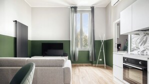 A modern living room with a sofa, a flat-screen TV, and a kitchen area with a stove and cabinets. - Navigli Riverside - One Bedroom Apartment, Sleeps 4 (Milano)