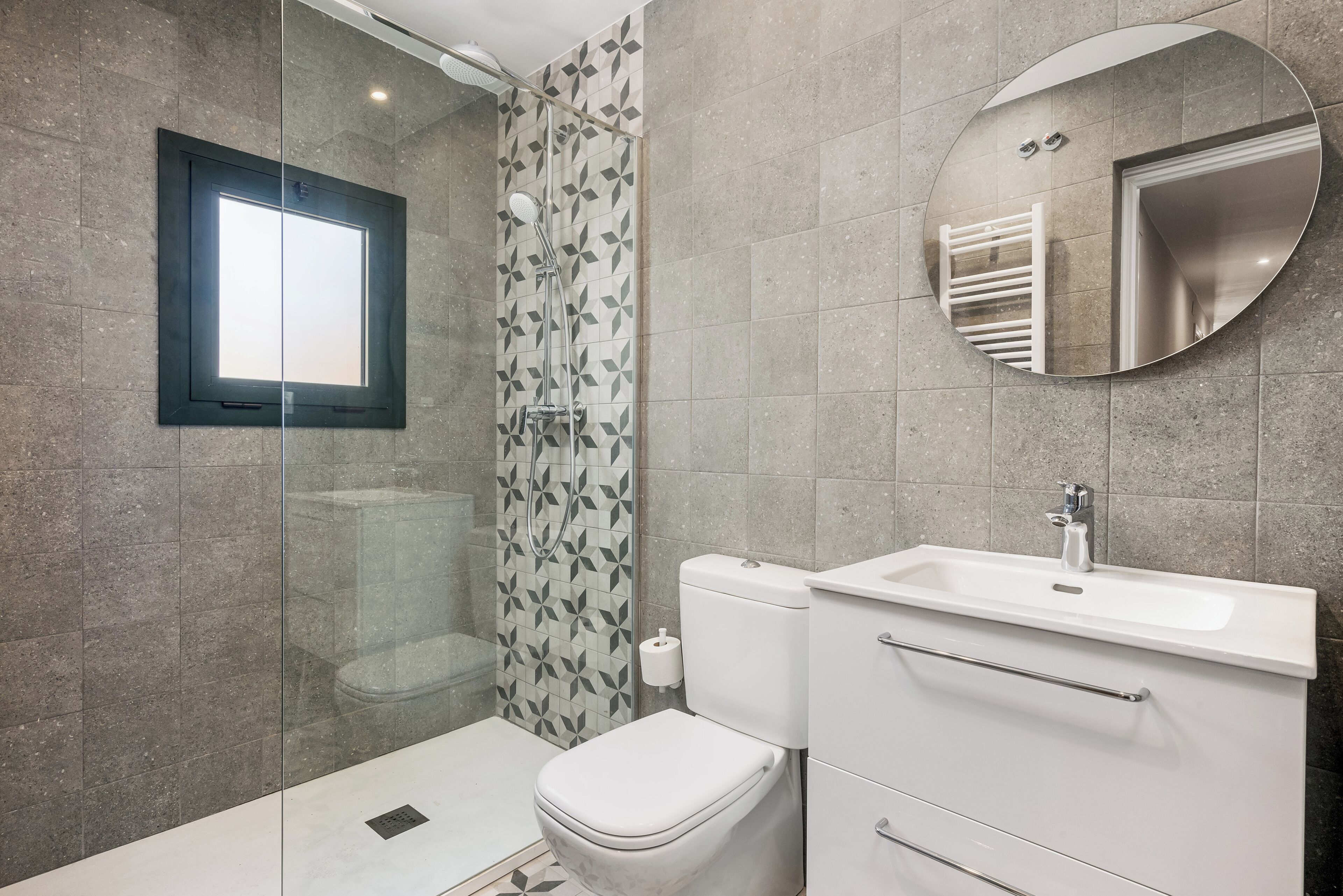 Un baño moderno con cabina de ducha de vidrio, inodoro, lavabo y espejo.