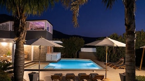 A modern outdoor pool area with lounge chairs and umbrellas, surrounded by palm trees and a stone wall. - Villa Amira - Castellammare Del ... (Castellammare del golfo)