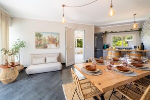 Un comedor con una mesa de madera dispuesta para seis personas, rodeada de sillas de mimbre, un sofá y un cuadro en la pared.