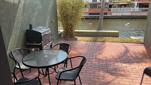 Un patio con una parrilla, una mesa y sillas, con vistas a un canal con patos.