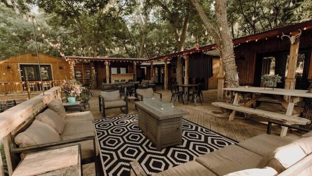 An outdoor patio area with wooden furniture, a patterned rug, and string lights.