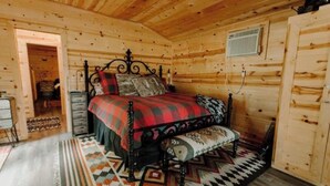 A wooden cabin bedroom with a bed, a nightstand, a dresser, and a patterned rug.