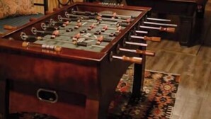 A room with a foosball table, a pool table, and a patterned rug.