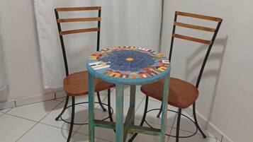 Una mesa redonda con una tapa de mosaico de colores, acompañada por dos sillas de madera con estructura metálica.
