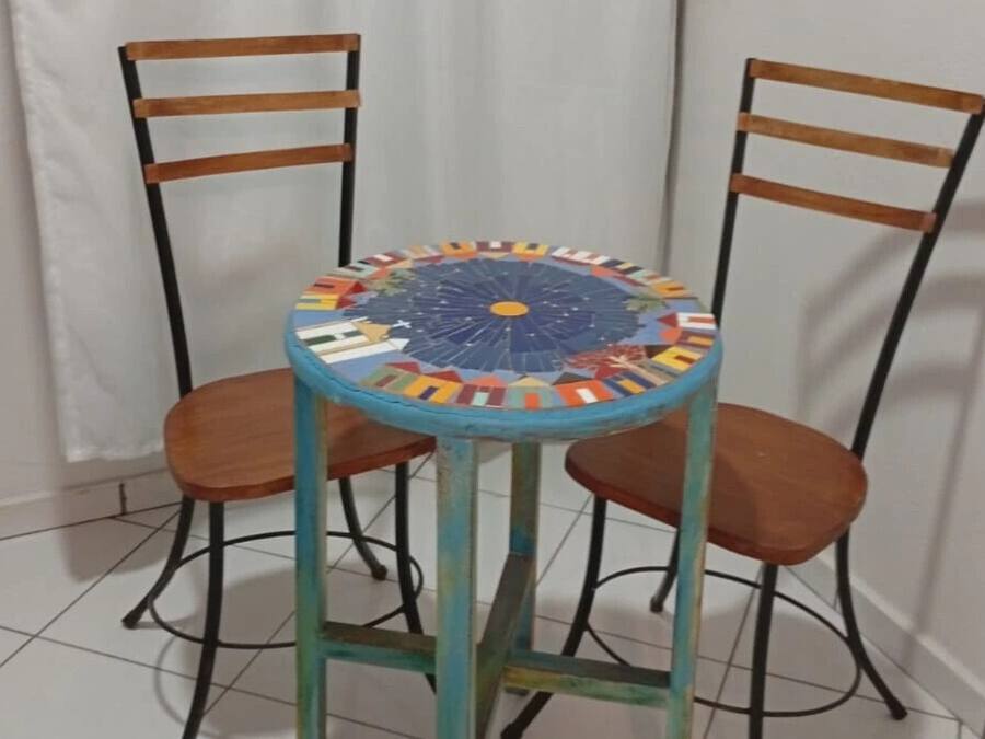 Una mesa redonda con una tapa de mosaico de colores, acompañada por dos sillas de madera con estructura metálica.