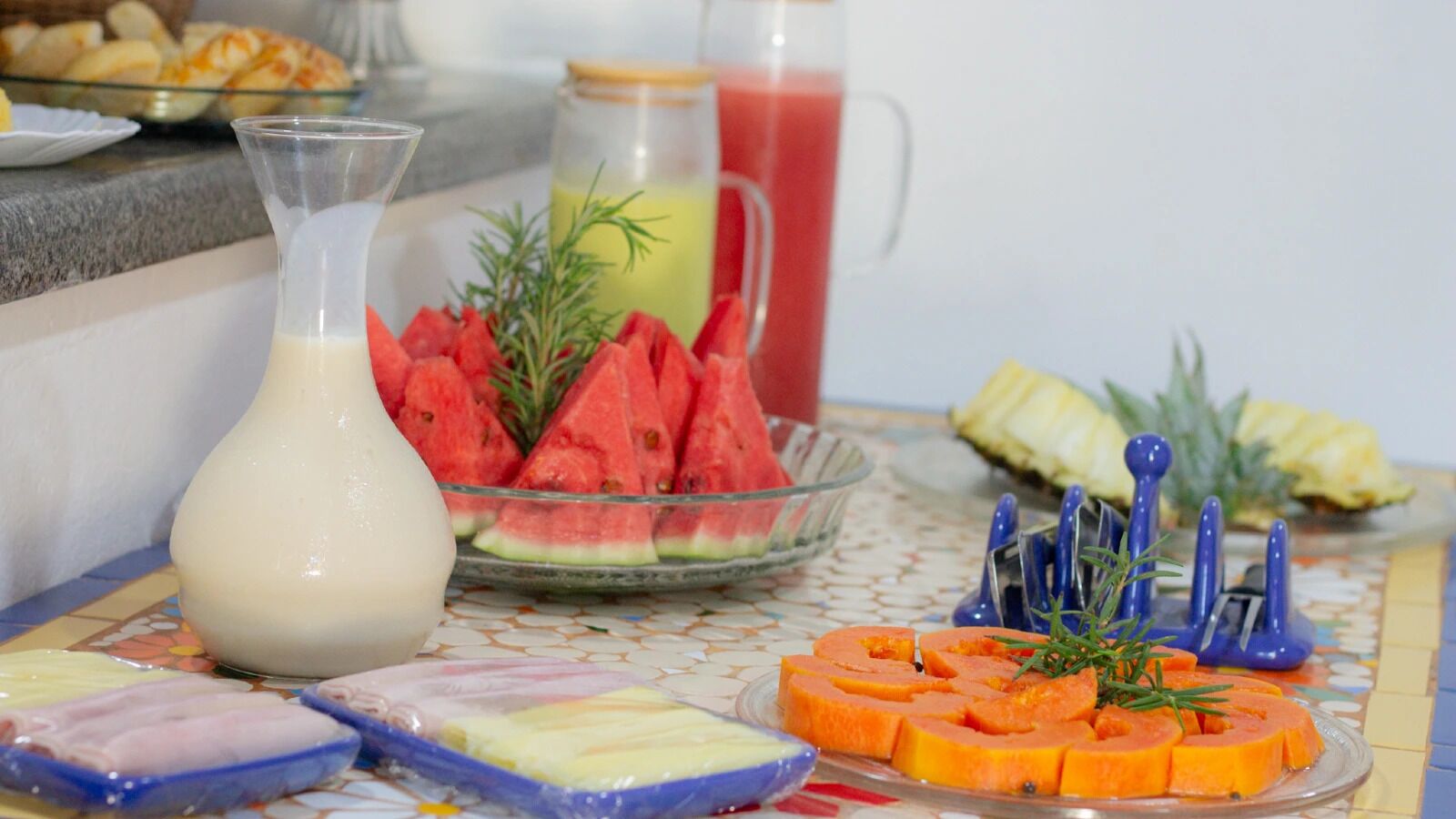 Una mesa de buffet con diversos alimentos, incluyendo zanahorias en rodajas, sandía y una jarra de leche.