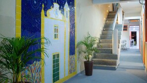 A hallway with a staircase, potted plants, and a colorful mural on the wall.