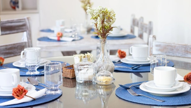 A dining table set with white plates, clear glasses, and a vase with white flowers.