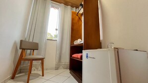 A small room with a chair, a white refrigerator, and a shelf with a red towel.