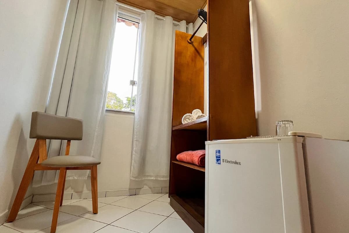 Um quarto pequeno com uma cadeira, um frigorífico branco e uma estante com uma toalha vermelha.