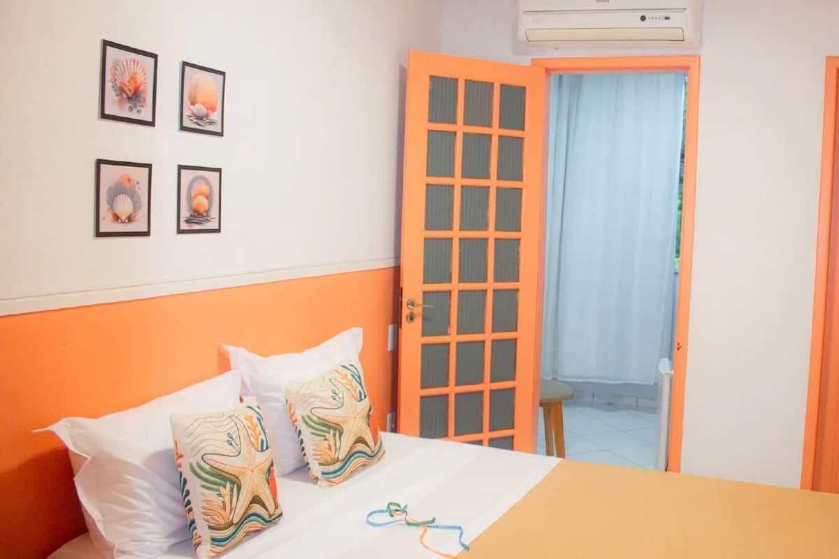 Quarto com uma cama, duas almofadas, janela com cortina e uma porta.