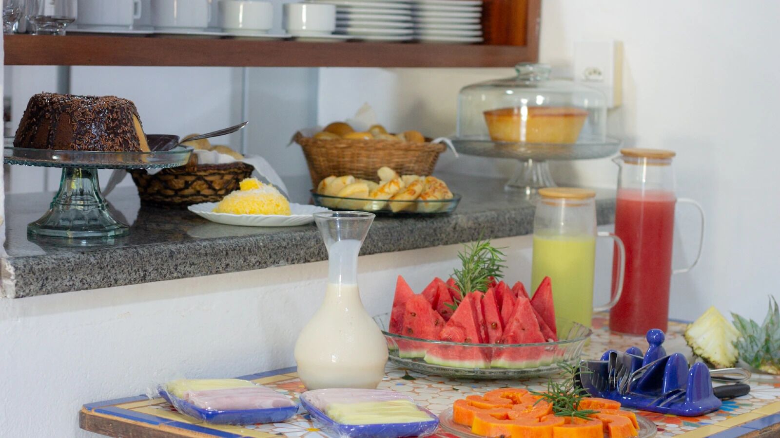 Buffet com diversos alimentos, incluindo bolo de chocolate, frutas e bebidas.
