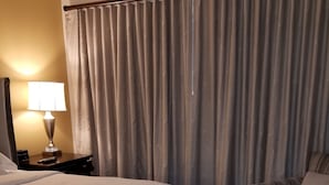 Habitación de hotel con una cama grande, una silla, una lámpara y una cortina.