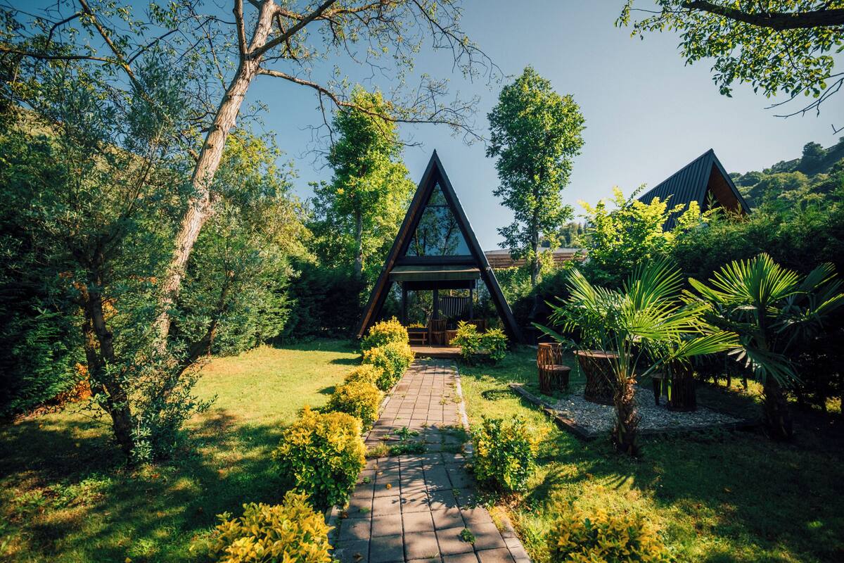 A triangular glass structure surrounded by lush greenery and a paved pathway leading to it.