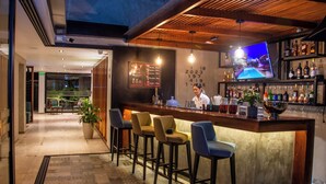 A bar area with a counter, stools, and a TV screen. There are bar stools, a bar counter, and a TV mounted on the wall. - GRAU BUSINESS HOTEL (Piura)