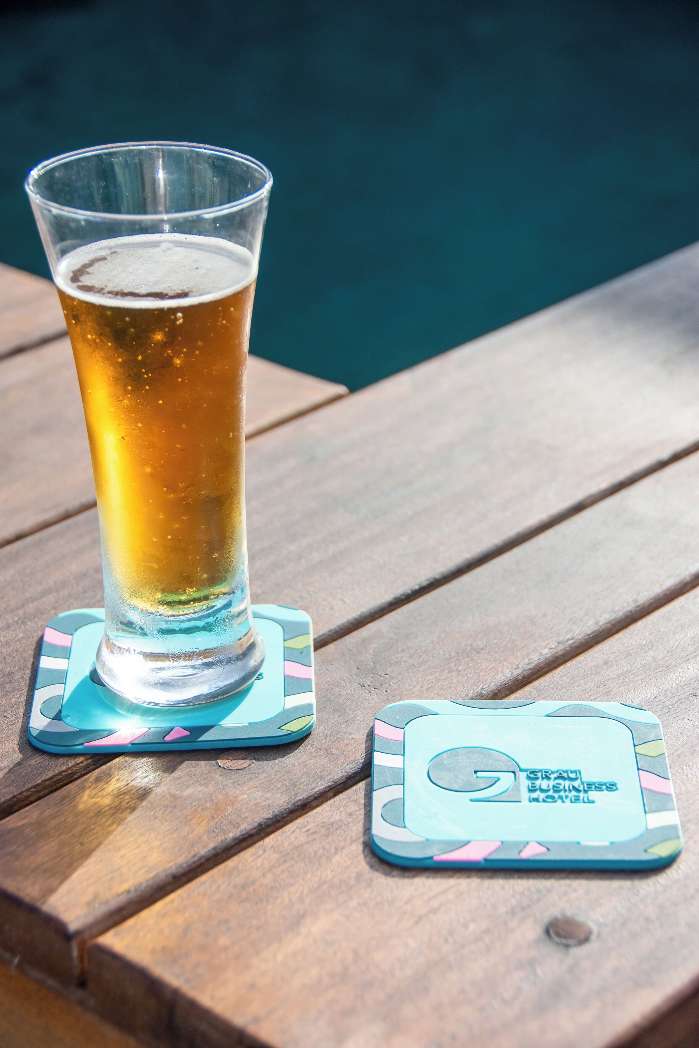 A glass of beer on a wooden table with a coaster and a business card.