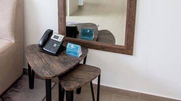 Une chambre d’hôtel avec un grand miroir, une table de chevet avec un téléphone et un panneau, un lit et une petite table de nuit avec une lampe.
