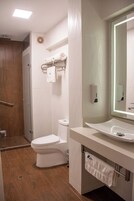 Un baño moderno con inodoro blanco, lavamanos con espejo y zona de ducha.