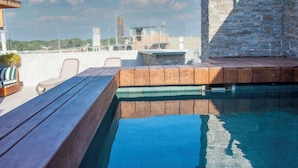 A rooftop pool with wooden deck seating and a stone wall. - GRAU BUSINESS HOTEL (Piura)
